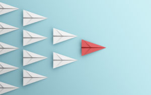 Red paper airplane leading white paper airplanes on a blue background