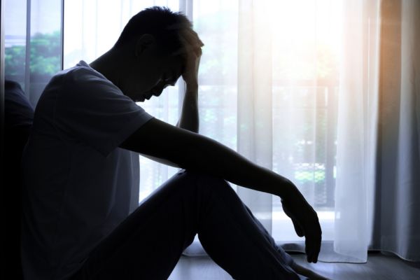 A person sitting in the corner of the room with their head on their hands in distress