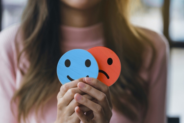 Hands holding a sad face hiding or behind happy smiley face