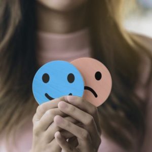 Hands holding a happy face with a sad face behind it